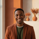 A happy young man in his mid-20s smiles at the camera, conveying satisfaction and trust. He has short dark hair and is wearin